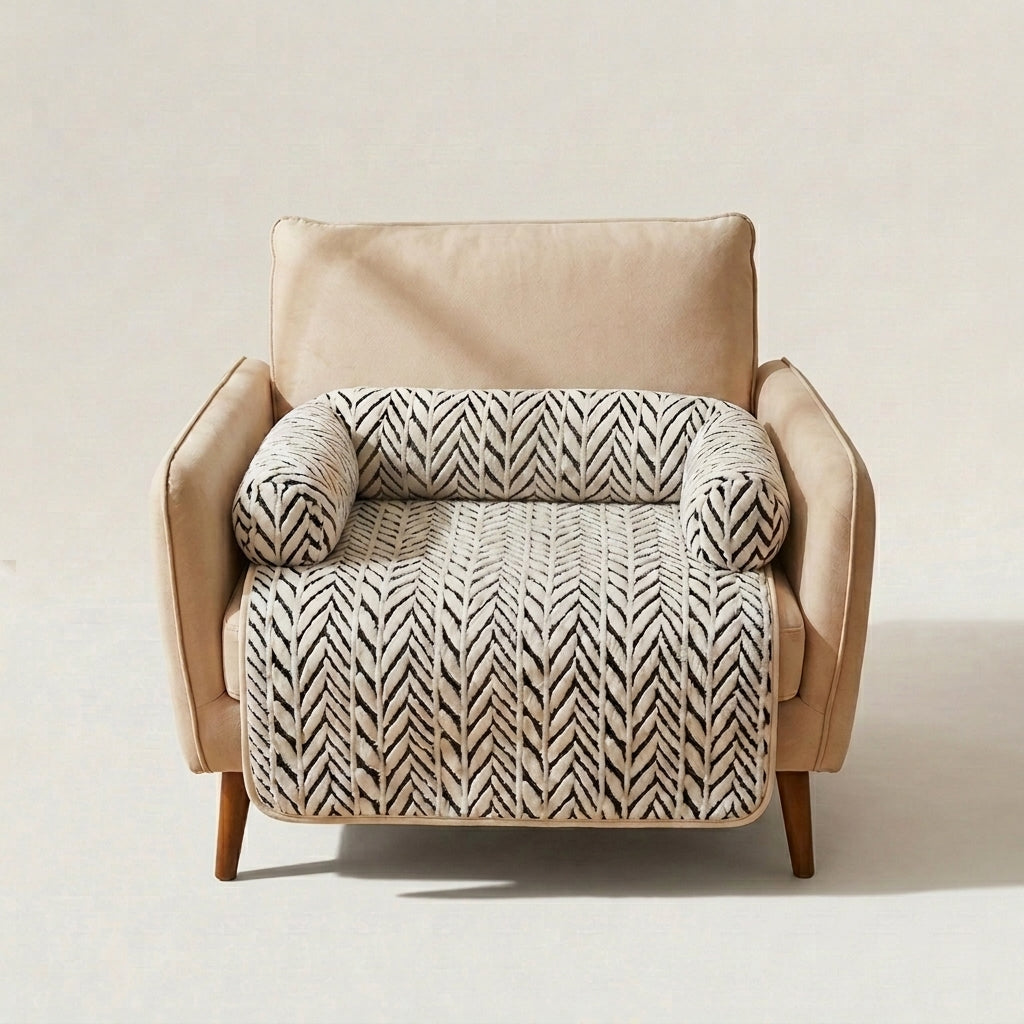 A beige upholstered armchair with a cream and black herringbone-patterned throw blanket draped across the seat and back, shown against a plain light beige studio background.