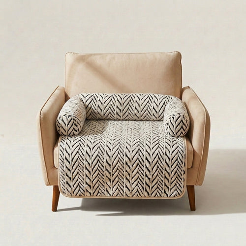 A beige upholstered armchair with a cream and black herringbone-patterned throw blanket draped across the seat and back, shown against a plain light beige studio background.