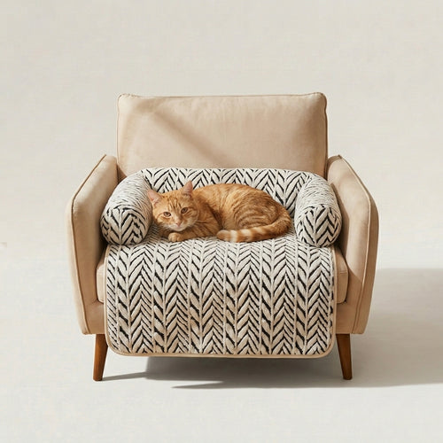 A beige upholstered armchair with wooden legs, styled with a cream and black herringbone-patterned pet bed and a sleeping orange tabby cat resting on top, set against a plain light beige studio background.