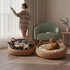 Two round woven pet beds with cushion tops are shown in a softly lit room. One cat lies on its back in the left bed, and an orange cat sits on its back in the right bed.