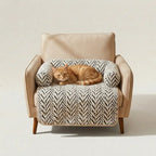 A beige upholstered armchair with wooden legs, styled with a white and black herringbone-patterned pet bed and a sleeping orange tabby cat on top, set against a plain beige studio background.